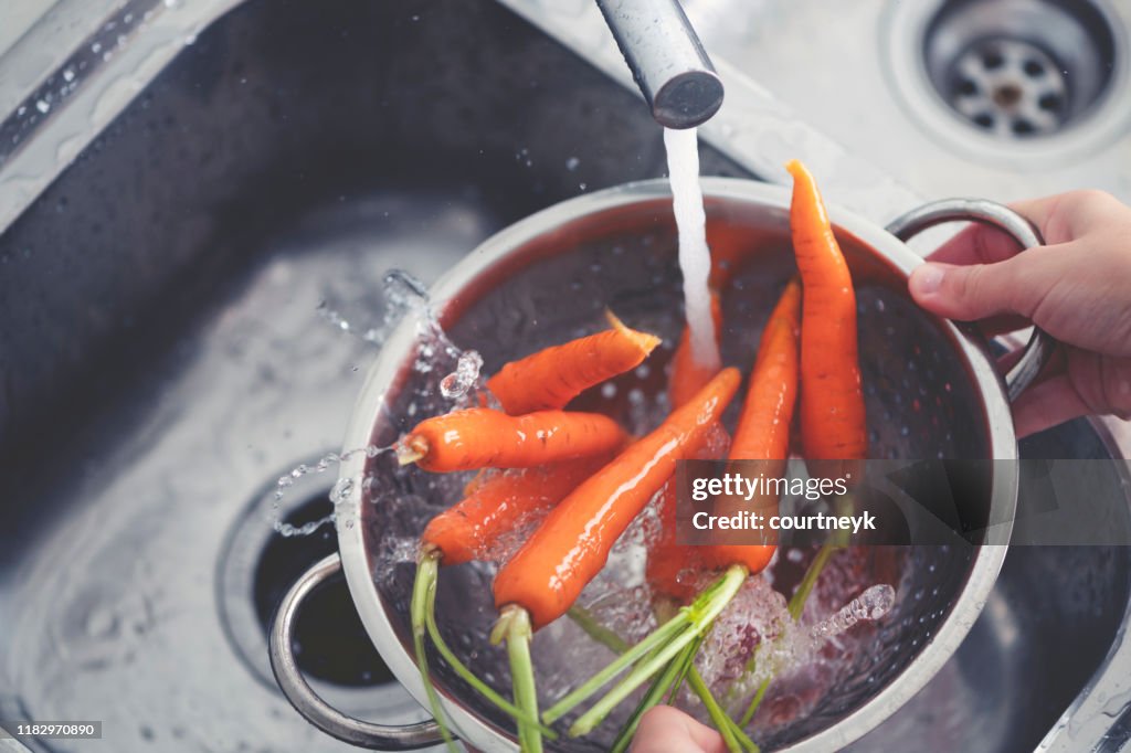 Woman washing carrots in the sink.