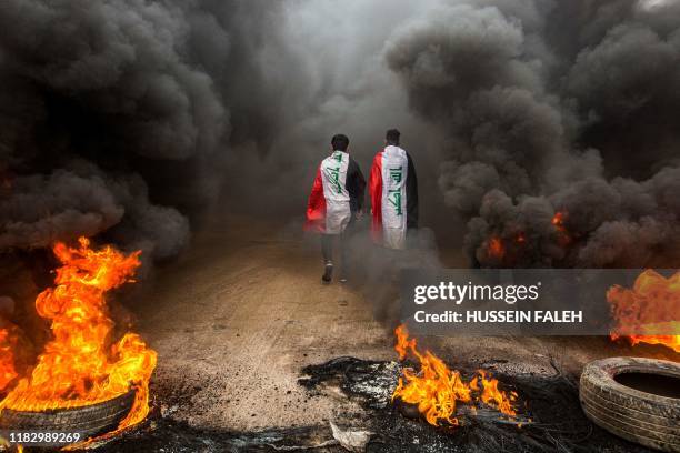 Anti-government protesters draped in Iraqi national flags walk into clouds of smoke from burning tires during a demonstration in the southern city of...