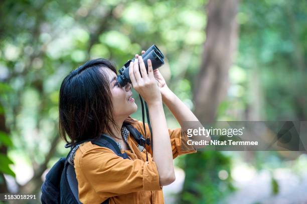 cheerful young asian woman bird watching through binoculars. nature lover concepts. - a ver pájaros fotografías e imágenes de stock