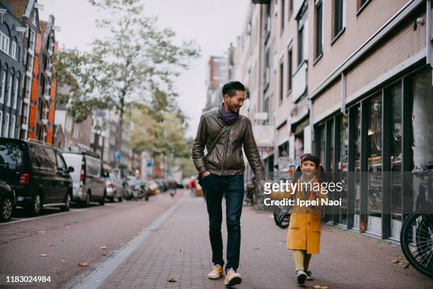 father and preschool girl walking on street in amsterdam - yellow coat stock-fotos und bilder