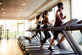 View of a row of treadmills in a gym with people.