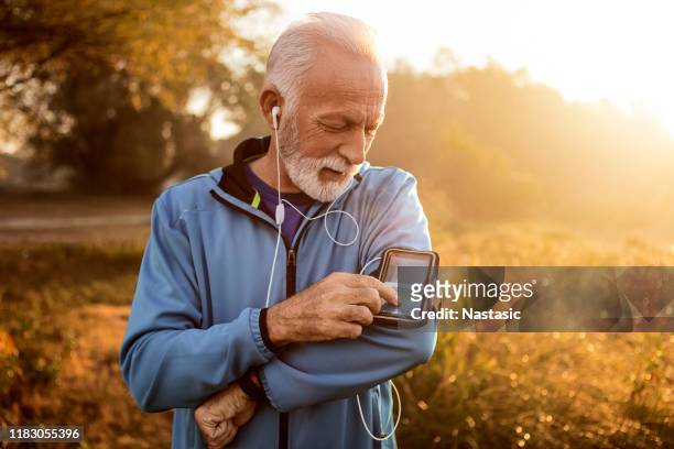 senior runner in nature with smart phone changing music - fitness app stock pictures, royalty-free photos & images