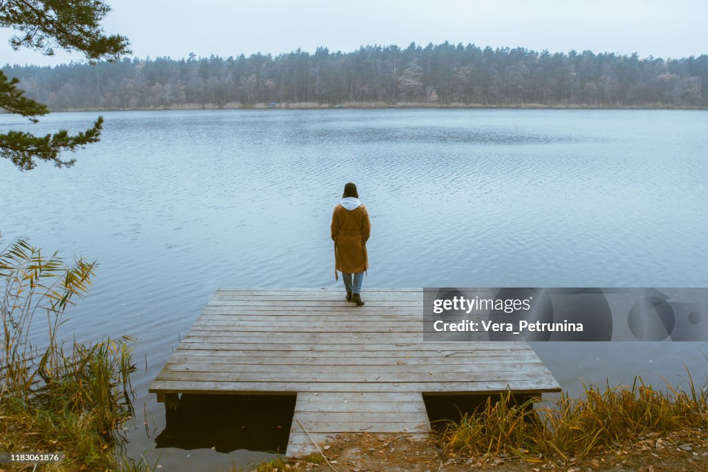 Autumn lake season woman in coat at wooden pier fall