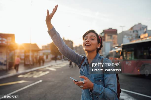 jonge vrouw die een taxi belt - uber stockfoto's en -beelden