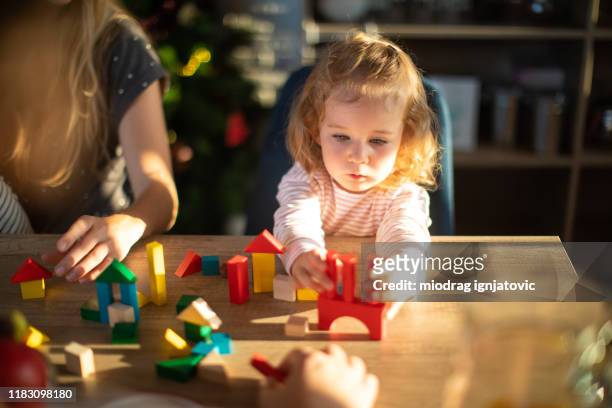 blond haar peuter meisje spelen met speelgoed blokken thuis - wooden table kids stockfoto's en -beelden