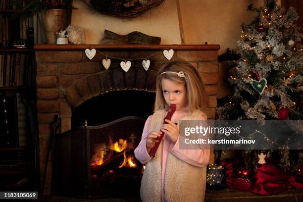 girl standing in front of a fireplace at christmas playing the recorder - recorder foto e immagini stock