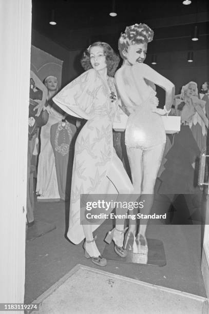 Female fashion model wearing a high-low asymmetrical wrap dress stands next to a cardboard cut out of Betty Grable during a fashion show in London on...