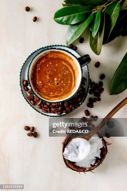 Bulletproof coffee. Keto diet coffee in blue ceramic cup with organic coconut cold press oil in wooden spoon with beans and green branch over white...