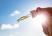 Hand holding dropper pipette with nice golden liquid D-vitamin against sun and blue sky on sunny day. Vitamin D keeps you healthy while lack of sun in winter, cure concept.