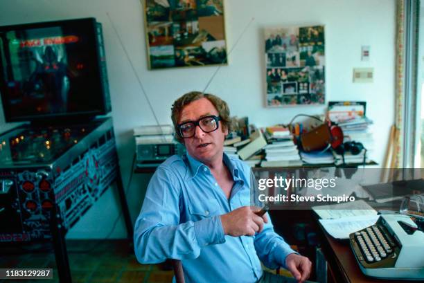 Portrait of English actor Michael Caine, a cigar in hand, as he sits in front of a typewriter at his home, Los Angeles, California, 1982. Visible in...