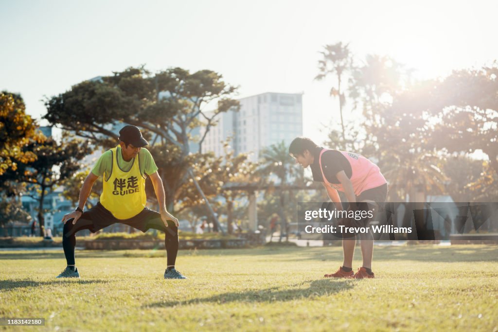 Blind marathon athlete stretching and warming up with his guide before competing