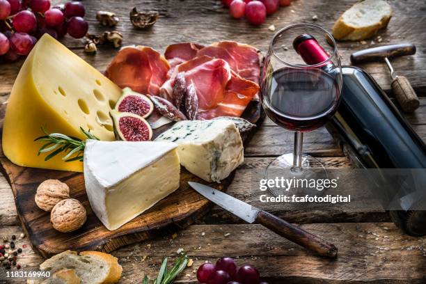 appetizer: red wine, cheese and cured ham on rustic wooden table - cheese platter stock pictures, royalty-free photos & images