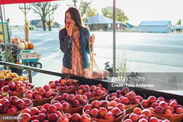 young woman shopping at outdoor fruit stand in autumn - adult female eating an apple stock pictures, royalty-free photos & images