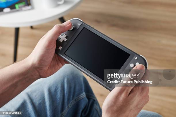 Detail of a person holding and playing a 2019 Nintendo Switch Lite handheld video games console with a Gray finish, taken on November 7, 2019.