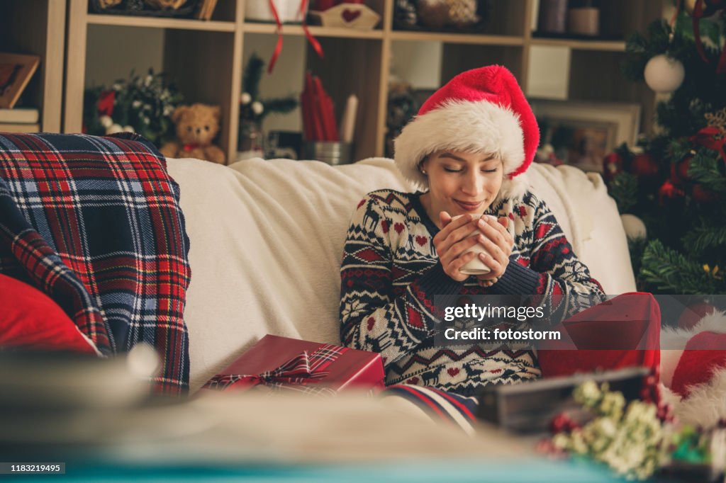 Mulher que aprecia o chá quente em um sofá durante o tempo do Natal