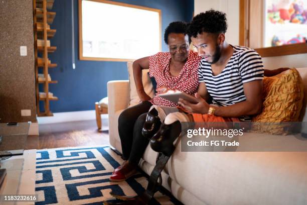 son/grandson using digital tablet with his mother/grandmother - amputee woman imagens e fotografias de stock