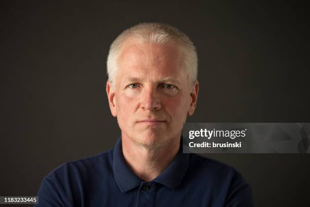 verticale de studio de plan rapproché d'un homme gris-cheveux de 55 ans dans un polo bleu sur un fond noir - rougeur photos et images de collection