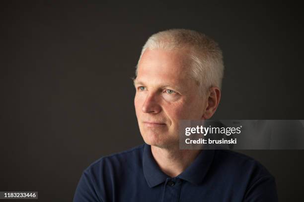 close-up studio portrait of a 55 year old gray-haired man in a blue polo shirt on a black background - three quarter front view stock pictures, royalty-free photos & images