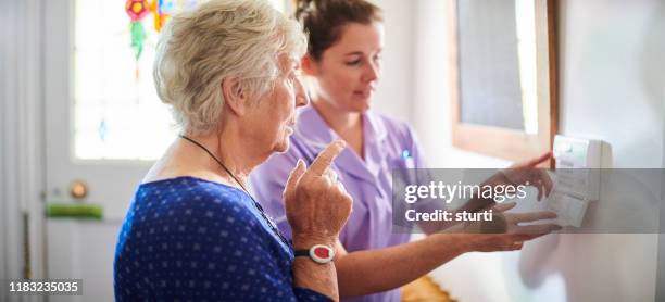 home verzorger toont senior vrouw haar alarm panel - nurse helping old woman at home stockfoto's en -beelden