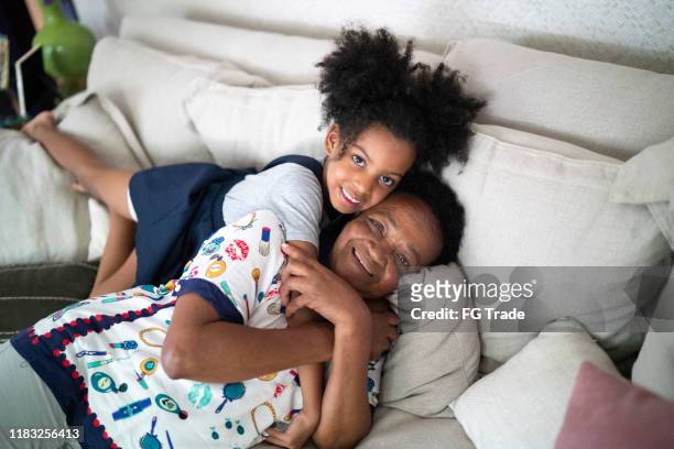 enkelin umarmt großmutter auf der couch, nach der rückkehr aus dem kindergarten - lying on back girl on the sofa stock-fotos und bilder