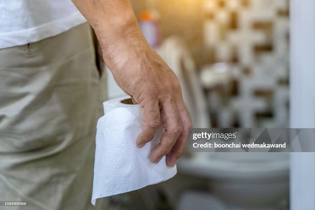 Man holding toilet tissue roll in bathroom looking at loo