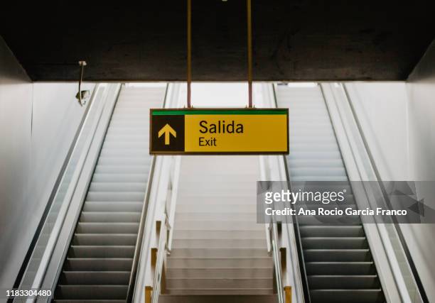 a yellow exit signal in a subway station.some blurry mechanical stairs on the back. - strassenunterführung stock-fotos und bilder