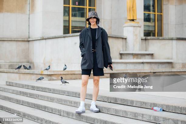 Model Ruinan Dong wears a brown printed bucket hat, bozy black striped blazer, black top, black shorts, and white Converse sneakers after the Rochas...