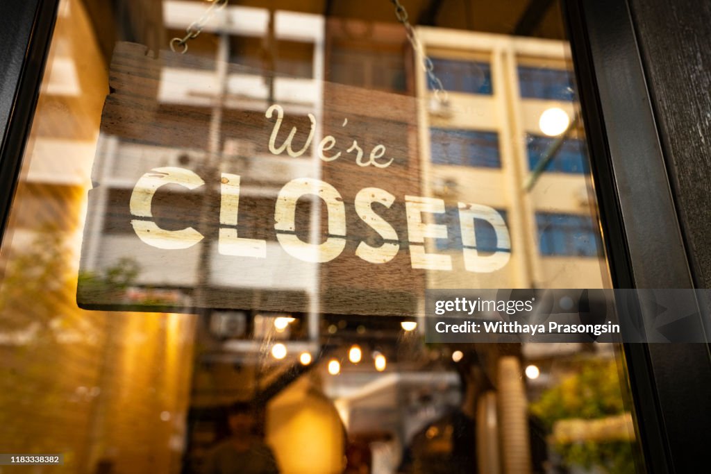 Closed sign hanging in business window by a string - crooked with glob of glue also attaching it to window