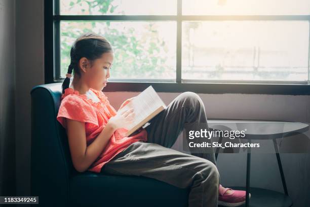 carina bambina asiatica che legge un libro nel soggiorno a casa, educazione e concetto di conoscenza - preteen foto e immagini stock