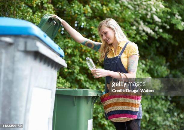 happy woman placing plastic bottle into recycling bin. - recylcebak stockfoto's en -beelden