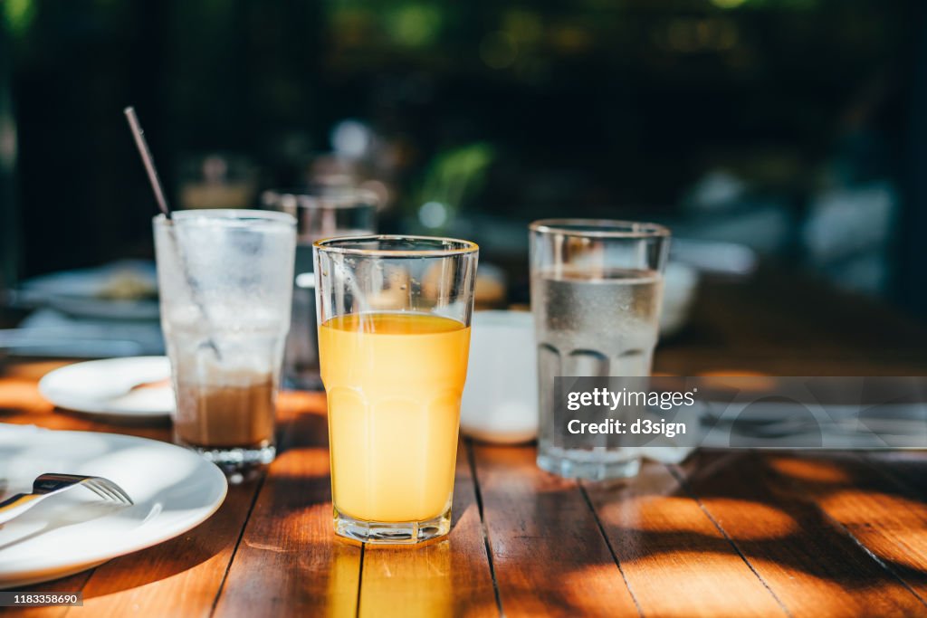 A glass of water, orange juice and coffee served on table in an outdoor restaurant against beautiful sunlight