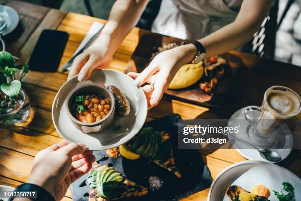 high angle view of woman passing platter of food to friend during brunch in an outdoor restaurant against beautiful sunlight - bangkok hotel stock pictures, royalty-free photos & images