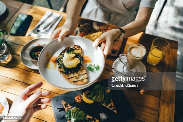 high angle view of woman passing platter of food to friend during brunch in an outdoor restaurant against beautiful sunlight - couple fine dining imagens e fotografias de stock