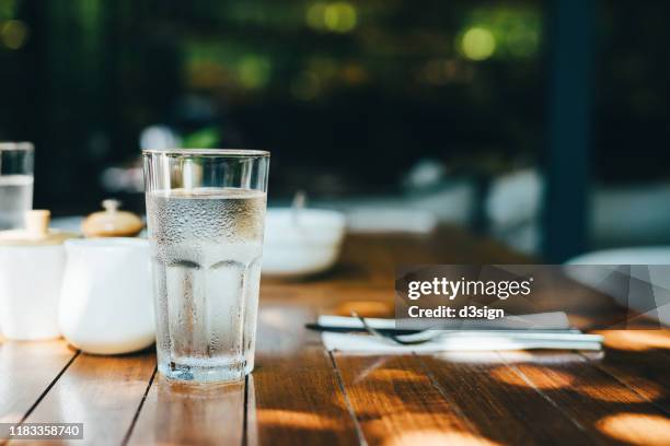 a glass of water served on table in an outdoor restaurant against beautiful sunlight - vaso de agua fotografías e imágenes de stock