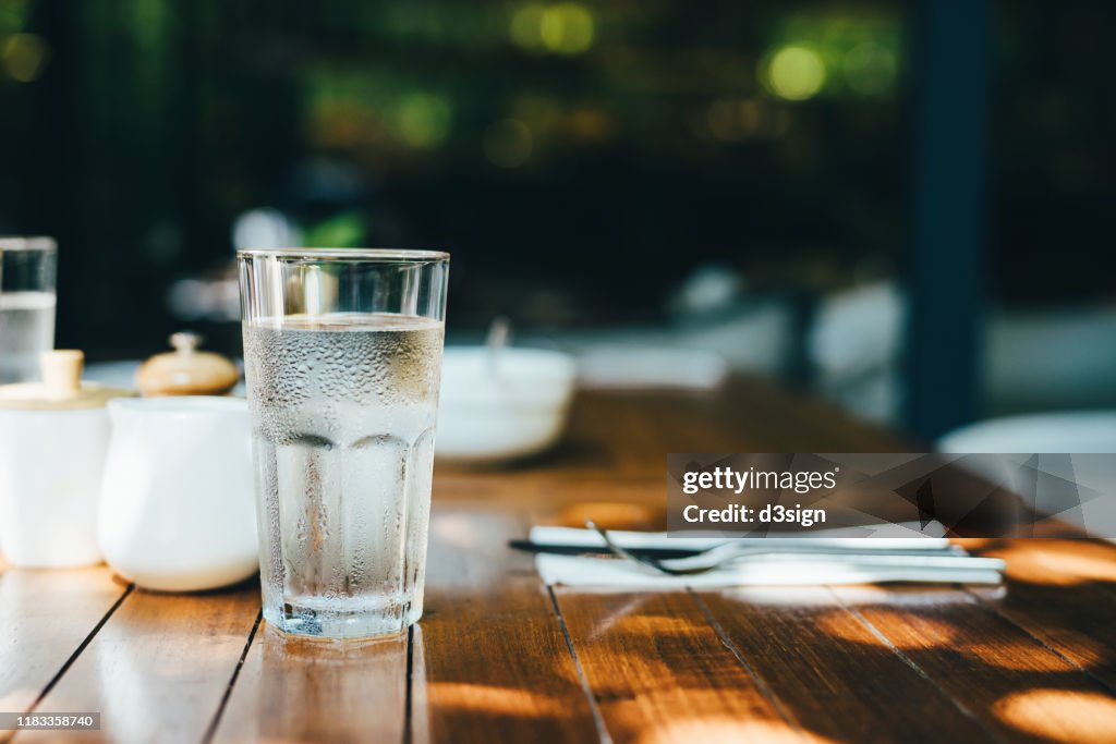 A glass of water served on table in an outdoor restaurant against beautiful sunlight