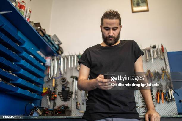 checking his social media in auto repair shop - repairman phone stock pictures, royalty-free photos & images