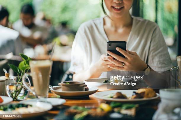 cropped image of woman using mobile phone while having brunch in an outdoor restaurant against beautiful sunlight - スマホ レストラン ストックフォトと画像