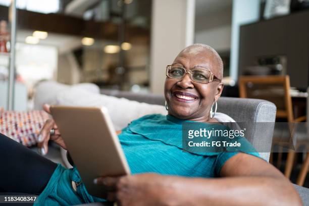 portrait of a senior woman using tablet at home - home inside relaxed facing camera stock pictures, royalty-free photos & images