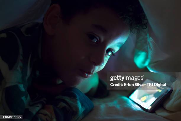 smart boy playing with smartphone hidden under the duvet - parental control stock-fotos und bilder