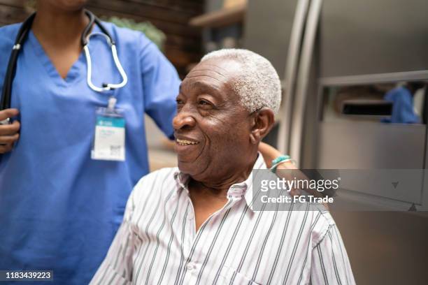 senior man sitting, nurse behind him - afro friends home stock pictures, royalty-free photos & images