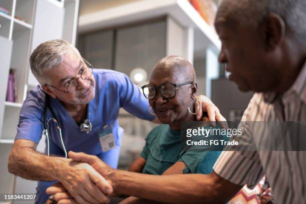 doctor greeting a senior couple - couple shaking hands with doctor stock pictures, royalty-free photos & images