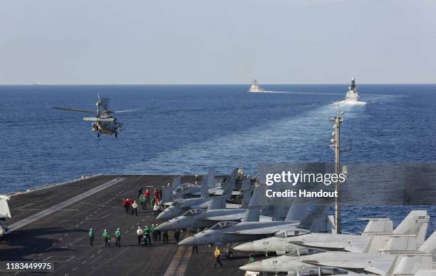 In this handout photo provided by the US Navy, The aircraft carrier USS Abraham Lincoln transits the Strait of Hormuz as an MH-60S Sea Hawk...