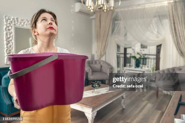 el techo de la casa está fluyendo - mujer sosteniendo el cubo mientras que las gotas de agua gotean desde el techo - fuga fotografías e imágenes de stock