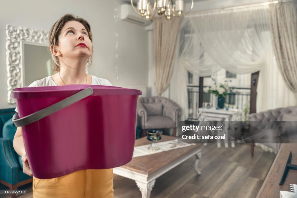 House Ceiling is Flowing - Woman Holding Bucket While Water Droplets Leak From Ceiling