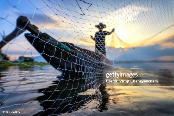 silhouette of asian fisherman on wooden boat casting a net for catching freshwater fish in nature river in the early morning. - mekong river stock-fotos und bilder