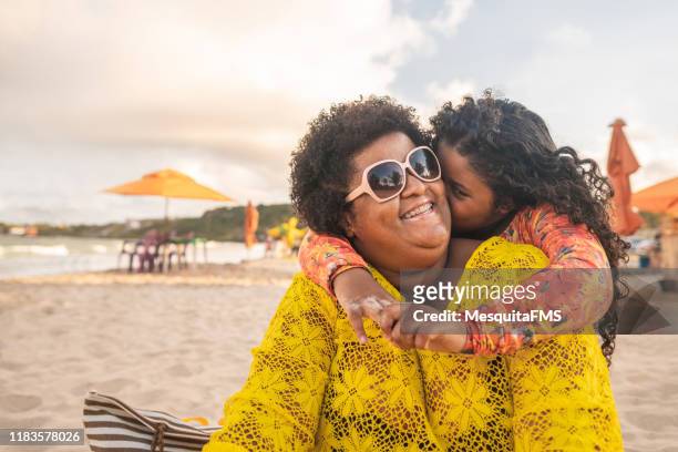 little girl kissing her mother and enjoying the beach - fat black girl stock pictures, royalty-free photos & images