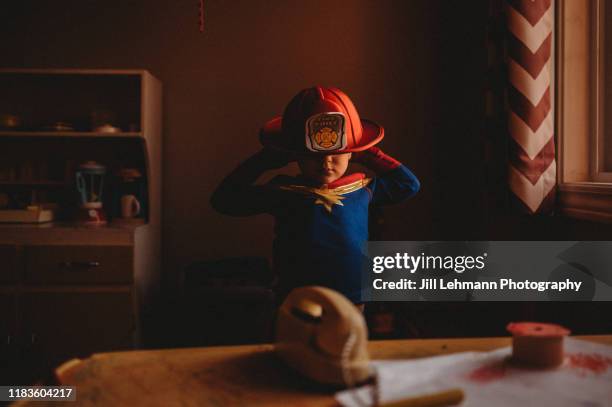 male toddler wears pajamas and a fire helmet in a window lit portrait at home - capacete de bombeiro - fotografias e filmes do acervo