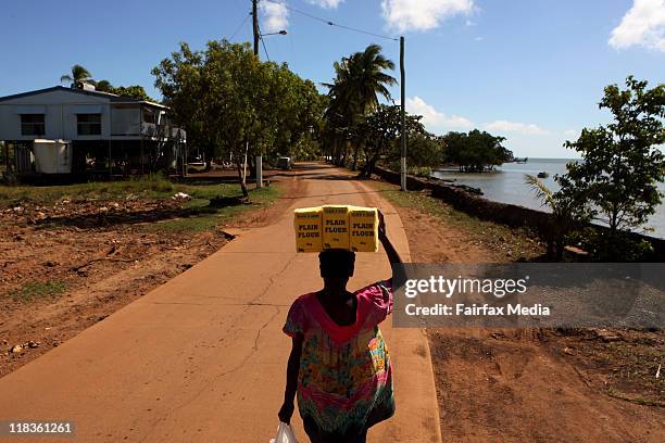 Woman walks home carrying flour on her head past a damaged sea wall on Saibai Island in the Torres Strait. King tides and strong winds have caused...