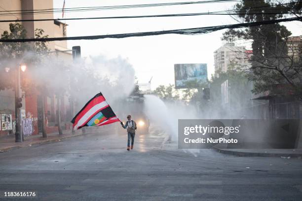 An anti-government demonstrator challenges a police water cannon spray during clashes with police in Santiago, Chile, Thursday, October 30, 2019.