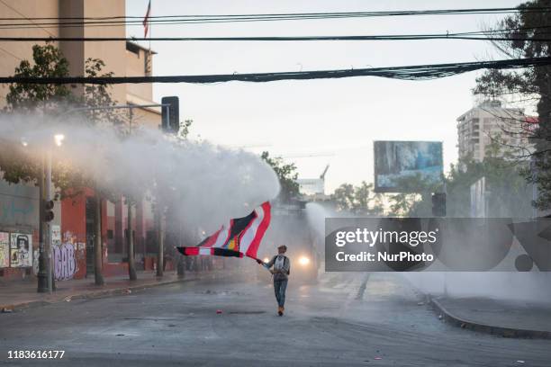 An anti-government demonstrator challenges a police water cannon spray during clashes with police in Santiago, Chile, Thursday, October 30, 2019.